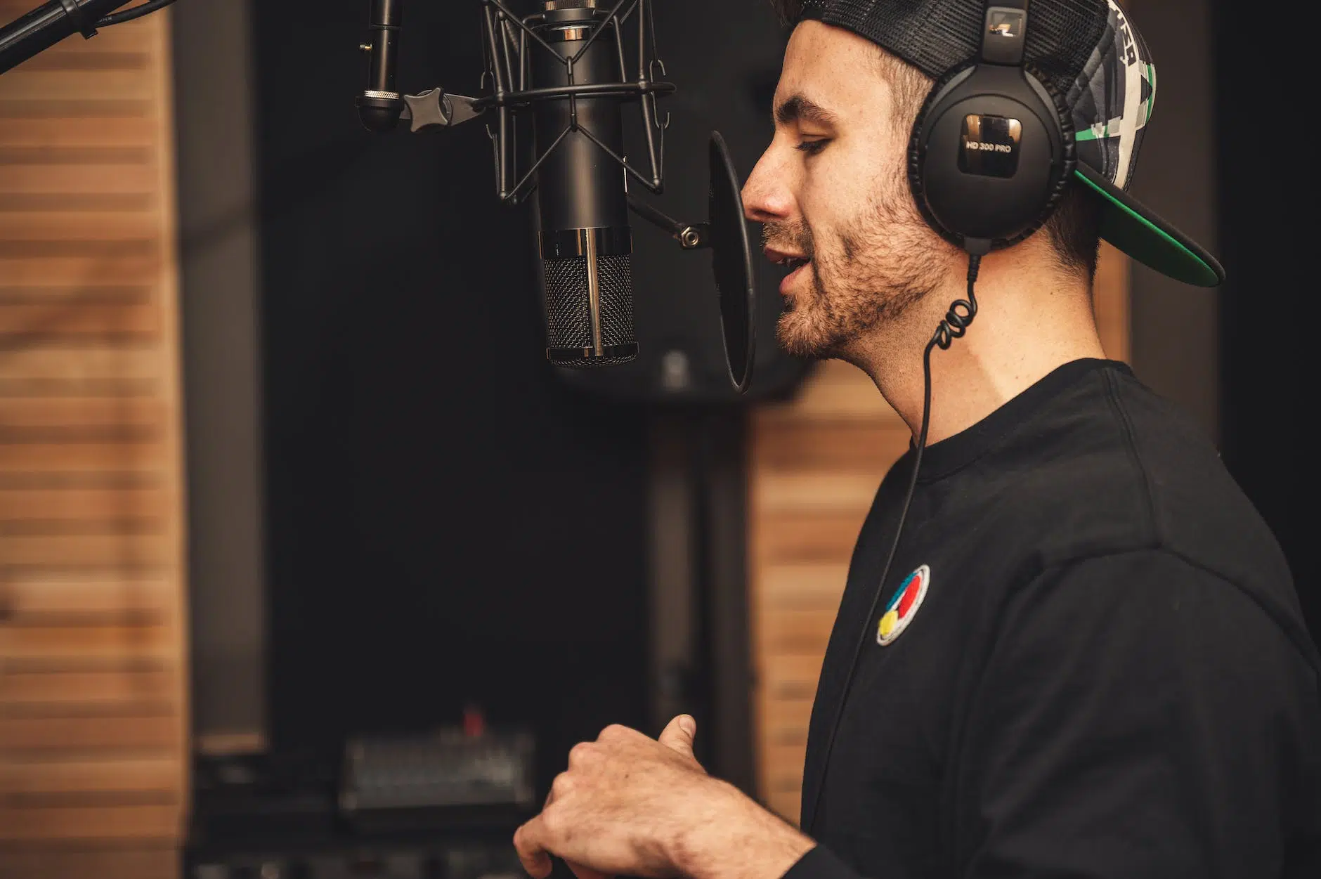 Hombre vestido de negro cantando en un estudio de música frente a un micrófono y con auriculares